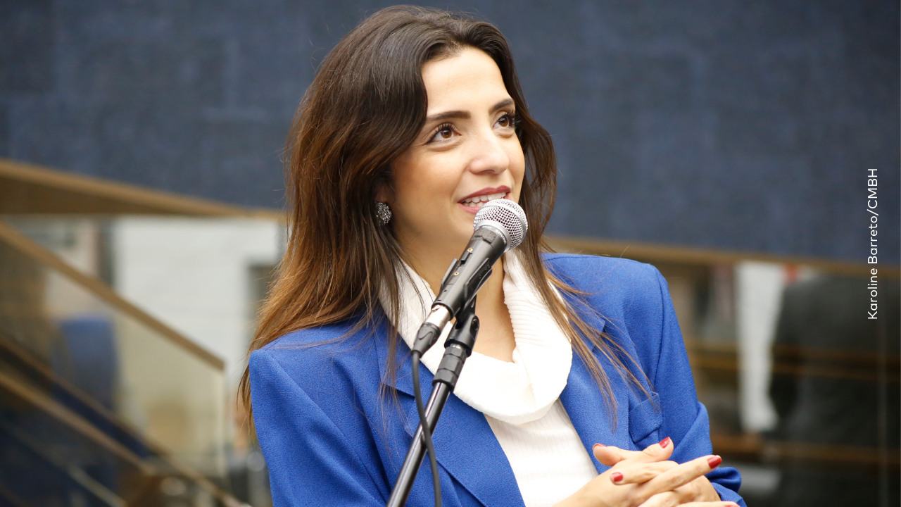 Marcela Trópia usando blazer azul falando ao microfone