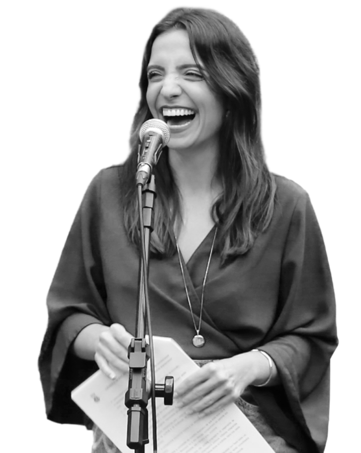 Marcela Trópia sorrindo atrás de um tripé com microfone