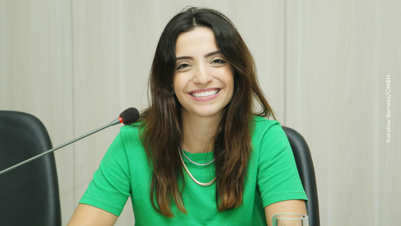 Marcela Trópia sorrindo para a câmera em primeiro plano com camisa verde