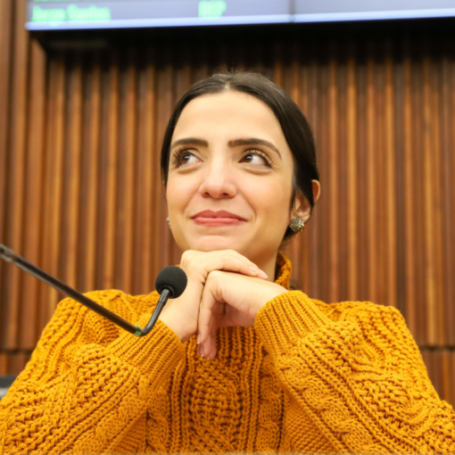 Vereadora Marcela trópia sorrindo apoiada nas mãos entrelaçadas sentada à Mesa Diretora da Câmara Municipal de Belo Horizonte